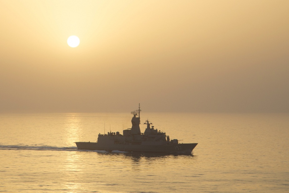 HMAS Perth sails through a misty sunset typical of the Middle East region in summer.