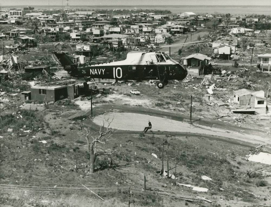 An RAN Wessex helicopter winches a civilian to safety during clean up operations