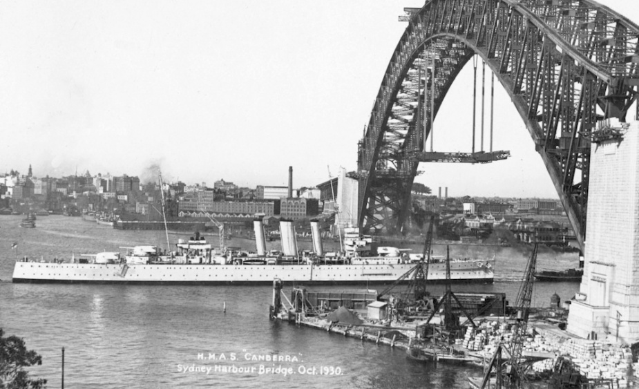 HMAS Canberra (I) passing under the still being constructed Sydney Harbour Bridge, October 1930.