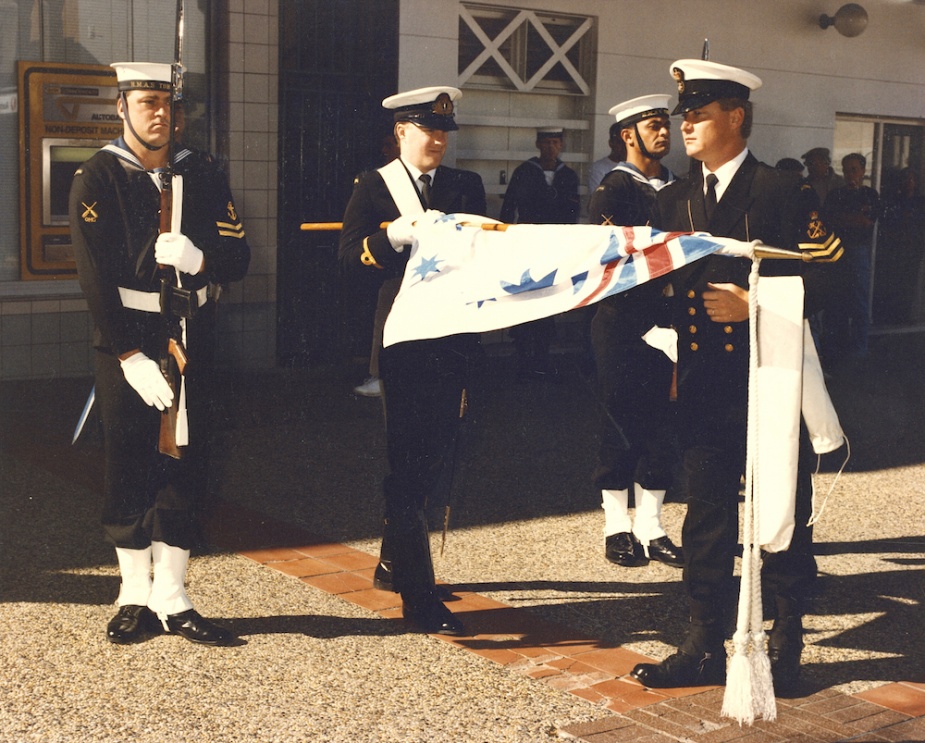 The Australian White Ensign is uncased by POQMG Tony Howard on the occasion of HMAS Tobruk's inaugural granting of Freedom of Entry into the City of Lake Macquarie on 9 August 1991. Visible in the escort party are: L-R: LSQMG Dean Faunt, SBLT MJ Kear and LSQMG Chris Bryant.