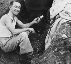 Wedmore, England. Informal portrait of Lieutenant Commander Leon Verdi Goldworthy, GC DSC GM and Bar, RANVR. The smiling Goldsworthy is holding a fuse he has just removed from the German Type C aerial magnetic mine in the trench behind him. Goldsworthy was one of several Australians of the RANVR attached to the Enemy Mining Section at HMS Vernon. (AWM  P03434.002)