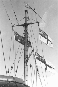 HMAS Bathurst (I)'s main mast proudly flying the Australian National Flag and multiple White Ensigns.