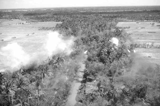 Helicopters in a landing zone as rockets explode near a tree line