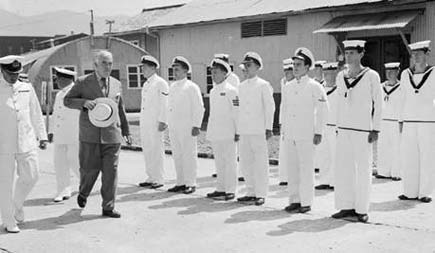 The Prime Minister Robert Menzies inspecting naval personnel at HMAS Commonwealth, the RAN shore based Station in Kure, Japan, 16 August 1950. Left to right: Commonwealth Boatswain B. McCarthy (facing away), Officer-in-charge of Tug Control; Mr Menzies; Stores Assistant G.W. Eves, Writer A.G. Carrolan, Lead Sick Berth Attendant A.R. Perberton, Stores Assistant B.B. Robertson, Officers Cook L.A.G. Wagner, Telegraphist P.T. Ryder and Signalman J.M. Dee.