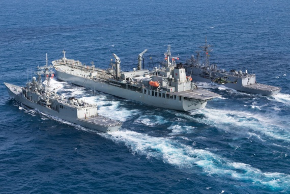 A MRH-90 Taipan helicopter from HMAS Adelaide conducts a vertical replenishment with HMAS Sirius, as it performs a dual replenishment at sea, refuelling HMAS Darwin (left) and HMAS Melbourne (right) simultaneously.