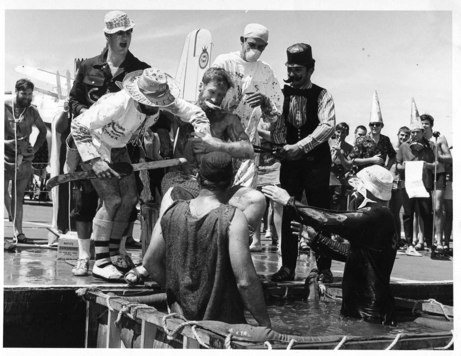 The Royal Barber and Royal Surgeon assist Vic Knowles in his transition from 'pollywog' to 'shellback'. (Note the trumpet and merriment in the background).